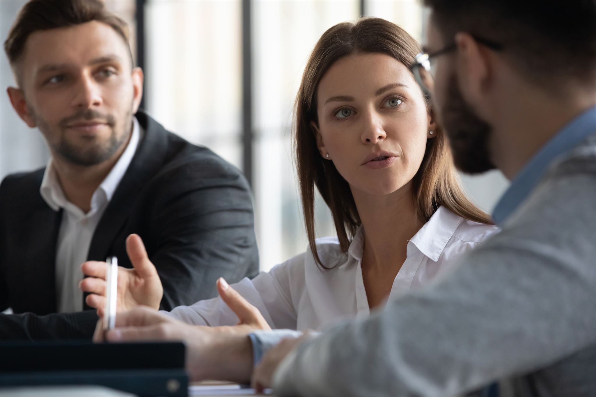People-in-business-attire-seated-at-table-in-conversation,-woman-in-center-of-two-men